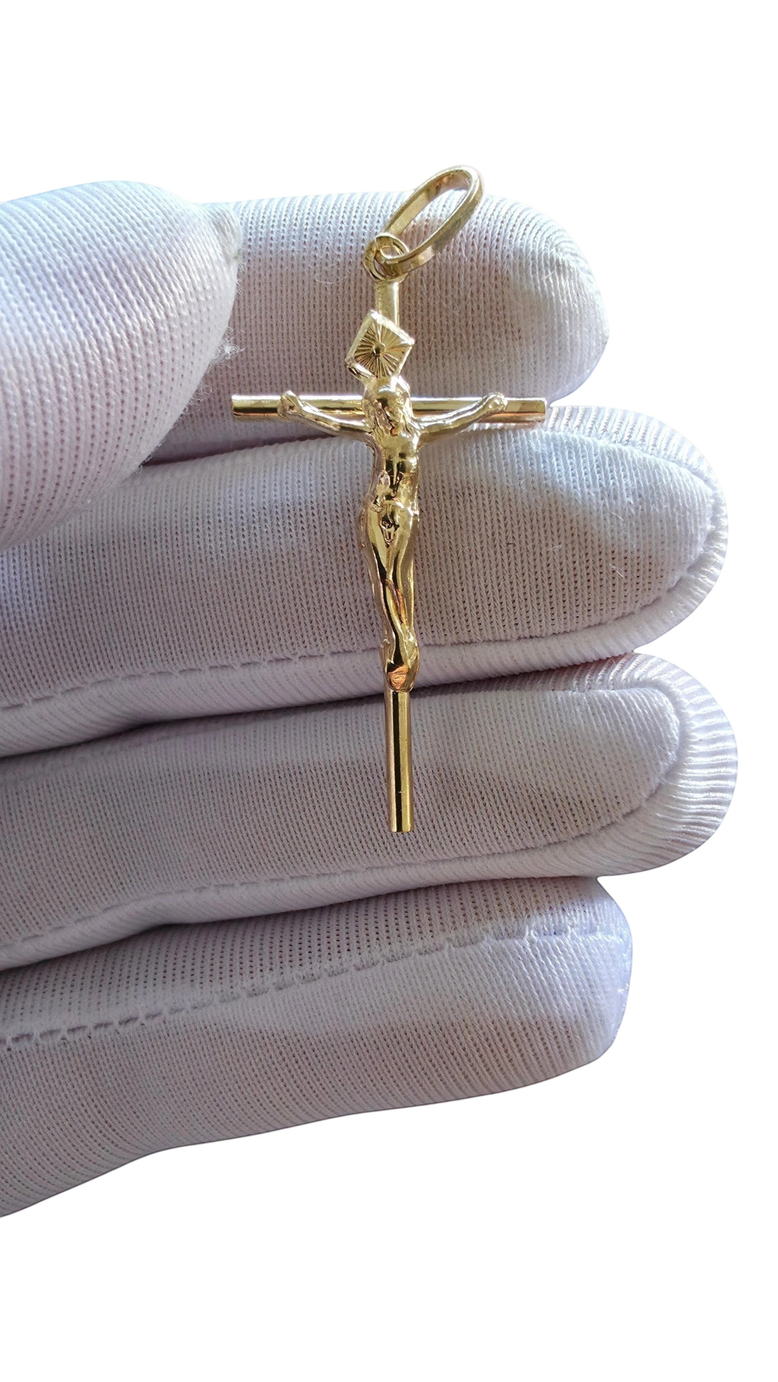 Medalha crucifixo em ouro amarelo 9k da Aurus Jóias, com 4cm de altura, segurada por uma mão com luva branca.